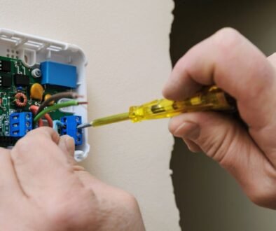 The man fixes the thermostat wiring.