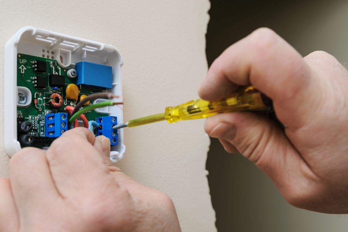 The man fixes the thermostat wiring.